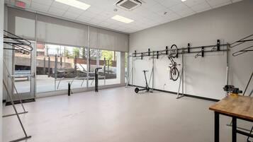 Una habitación amplia con ventanas grandes, una mesa de madera y varias bicicletas y scooters colgados en la pared.