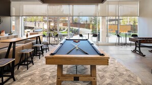 A pool table with stools, a foosball table, and a bar area with stools. - Landing Apartments at Five Points South (Birmingham)