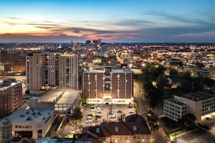 A cityscape at dusk with a prominent hotel featuring multiple floors, a parking lot, and a view of the surrounding urban area.