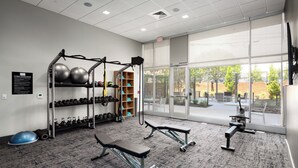 A gym with weightlifting equipment, benches, and a view of the outdoors through large windows. - Landing Apartments at Five Points South (Birmingham)