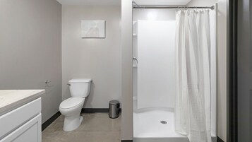 A bathroom with a toilet, a shower with a white curtain, and a marble countertop.