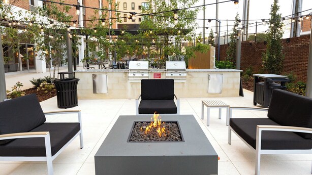 An outdoor patio with a central fire feature, seating, and a grill area. - Landing Apartments at Five Points South (Birmingham)