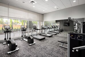 Une salle de sport équipée de tapis de course, d’appareils de musculation et d’un banc.