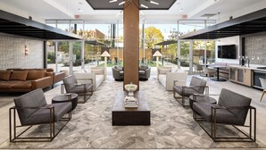 A spacious lobby with modern furniture, a central column, and a view of the outdoor area. - Landing Apartments at Five Points South (Birmingham)