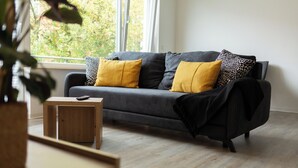 A modern living room with a grey sofa, wooden coffee table, and a view of greenery through a window. - BEST STAY: CITYAPPARTMENT in Hünfeld, WLAN, SmartTV, balcony, central & quiet (Hünfeld)
