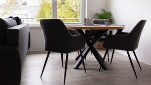 A modern dining area with a wooden table and black chairs, a grey sofa, and a view of trees through a large window. - BEST STAY: CITYAPPARTMENT in Hünfeld, WLAN, SmartTV, balcony, central & quiet (Hünfeld)