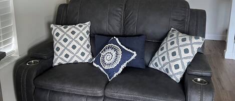 A dark leather sofa with patterned cushions, a potted plant, and a framed artwork on the wall.