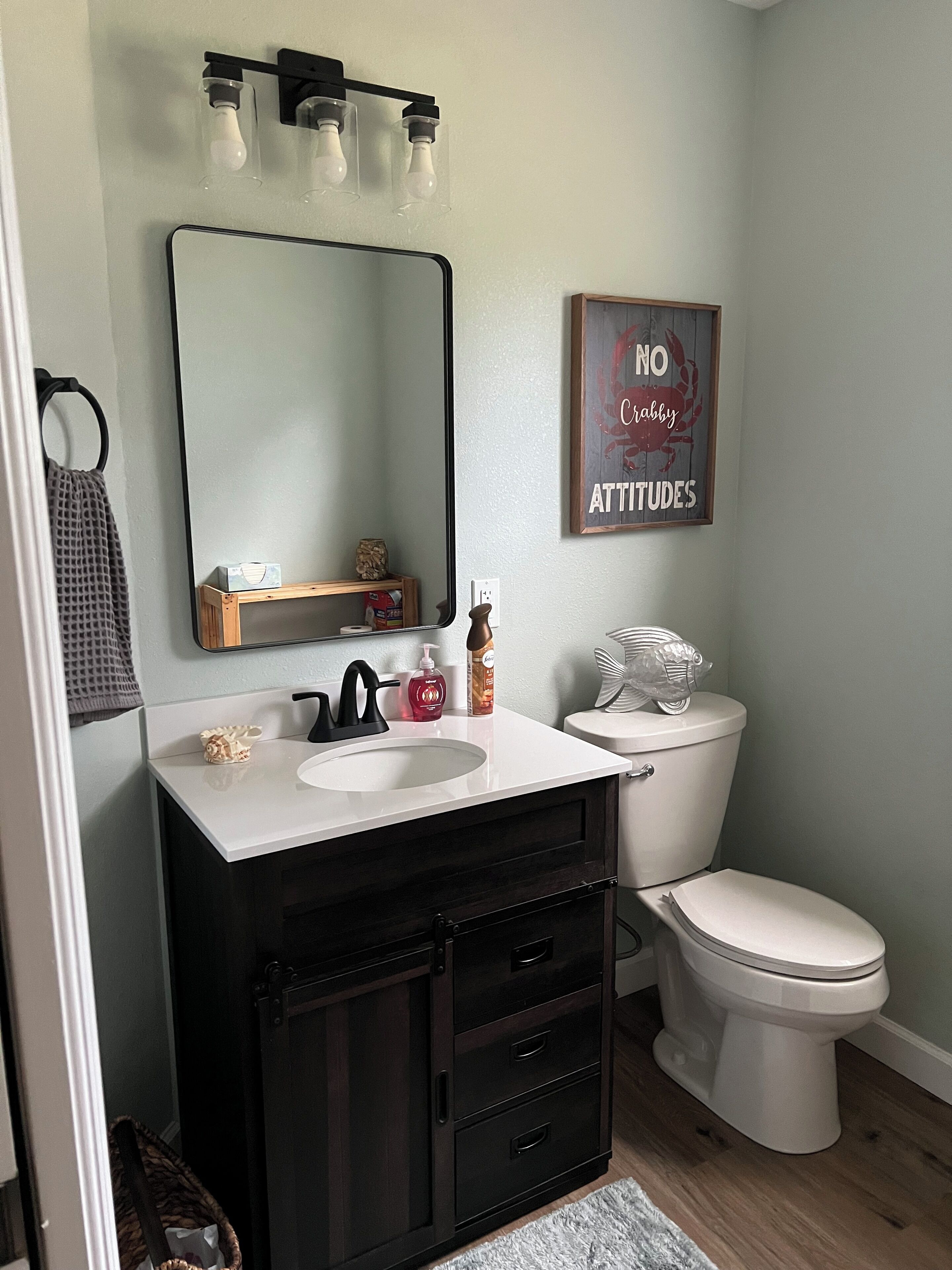 A bathroom with a white sink, dark wooden vanity, a mirror, a toilet, and a wall-mounted light fixture.
