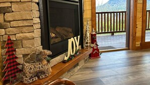 Una chimenea de piedra con una pantalla negra, un letrero que dice 'JOY' y adornos navideños.