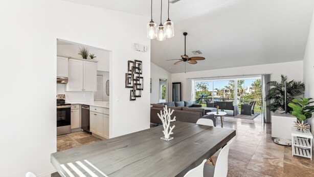 A modern kitchen with white cabinets and a dining area with a dark wooden table and white chairs. - Beachside Retreat: 2BD/2BA Gym + Boat Lift + SHARED Pool! (Fort Myers Beach)