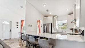 A modern kitchen with white cabinets, a stainless steel refrigerator, and a large island with bar stools. - Beachside Retreat: 2BD/2BA Gym + Boat Lift + SHARED Pool! (Fort Myers Beach)