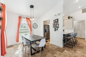 Une cuisine moderne dotée d’un four encastré, d’un réfrigérateur et d’un coin repas avec une table sombre et des chaises blanches.
