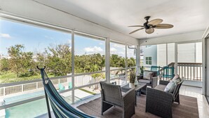 A spacious balcony with a pool, wicker furniture, and a ceiling fan. - Beachside Retreat: 2BD/2BA Gym + Boat Lift + SHARED Pool! (Fort Myers Beach)