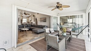 A spacious living area with a sectional sofa, a dining table with wicker chairs, a hammock, and ceiling fans. - Beachside Retreat: 2BD/2BA Gym + Boat Lift + SHARED Pool! (Fort Myers Beach)