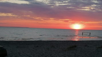 Una playa con un atardecer, mar tranquilo y un banco.