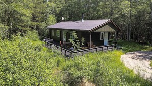 Mökki, jossa on kuisti, ja sen ympärillä tiheä metsä.
