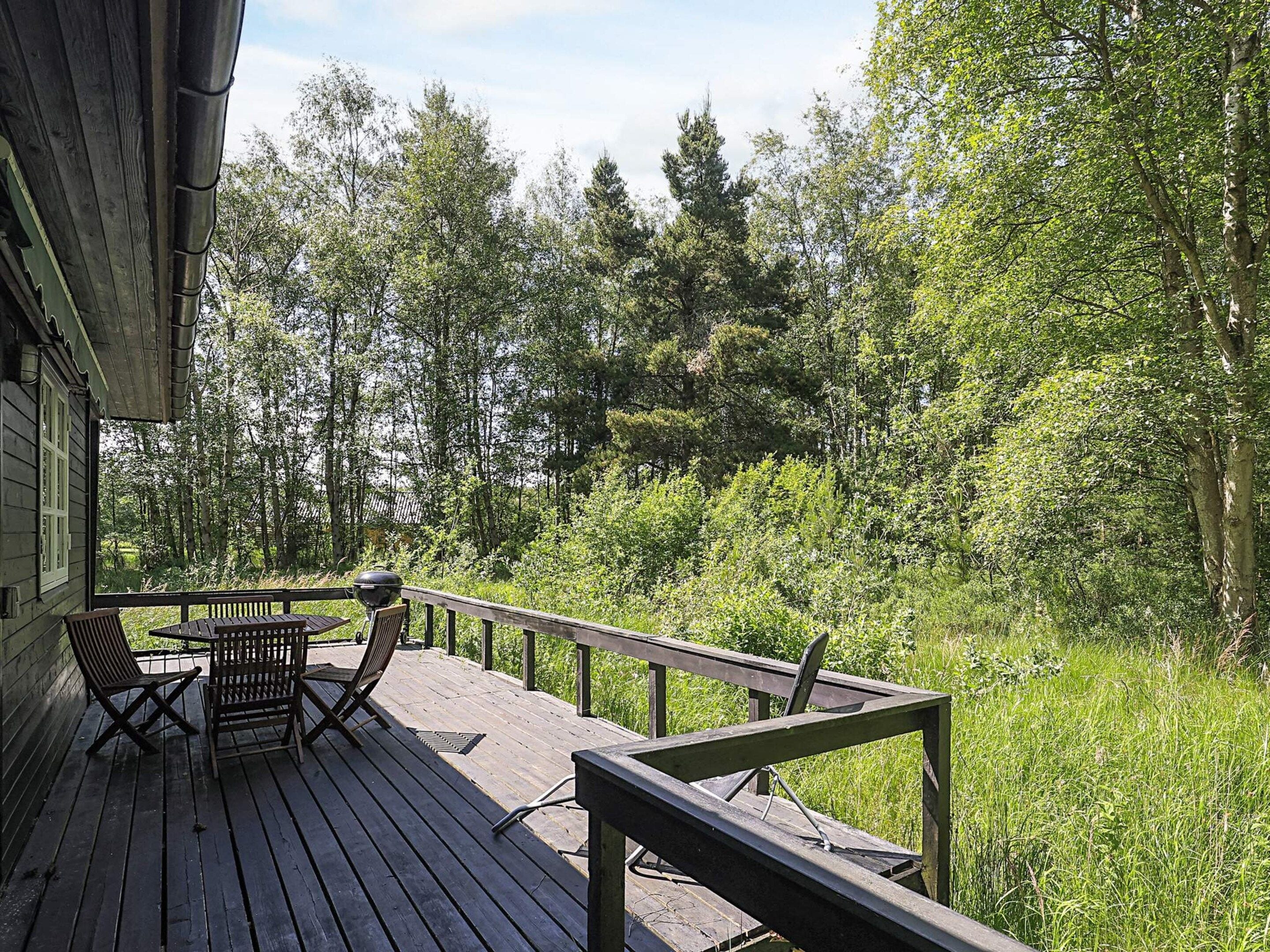 Un patio in legno con mobili da esterno, circondato da una fitta foresta.