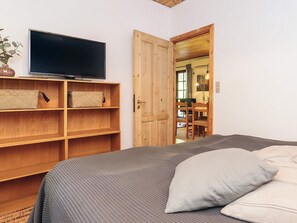 Une pièce avec un lit, un téléviseur posé sur une étagère et une porte en bois donnant sur une autre pièce.