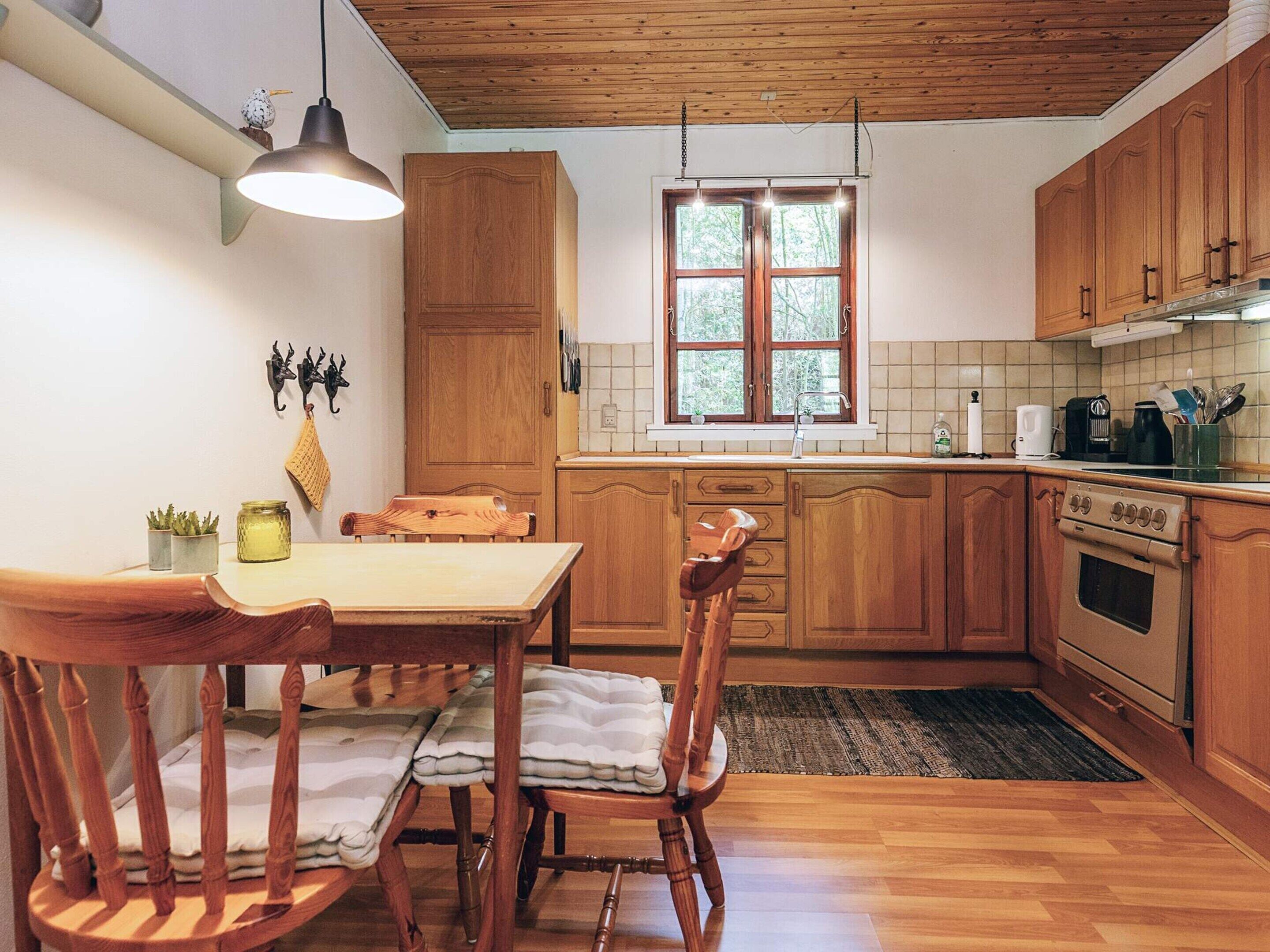 Una cocina con armarios de madera, una mesa de comedor, sillas, una lámpara colgante, una ventana y una estufa.