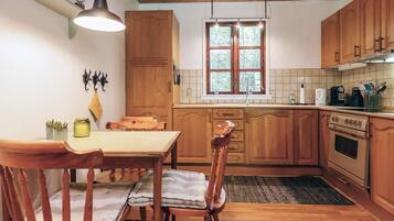 Una cocina con armarios de madera, una mesa de comedor, sillas, una lámpara colgante, una ventana y una estufa.