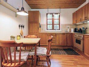 Une cuisine avec des meubles de rangement en bois, une table à manger, des chaises, un luminaire suspendu, une fenêtre et une cuisinière.