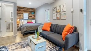 Un salon moderne avec un canapé gris, un lit agrémenté d’oreillers orange et un mur en bois rustique.
