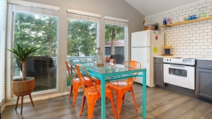 Une cuisine moderne avec une table à manger en verre et des chaises orange, un réfrigérateur blanc et un mur de fond en briques.