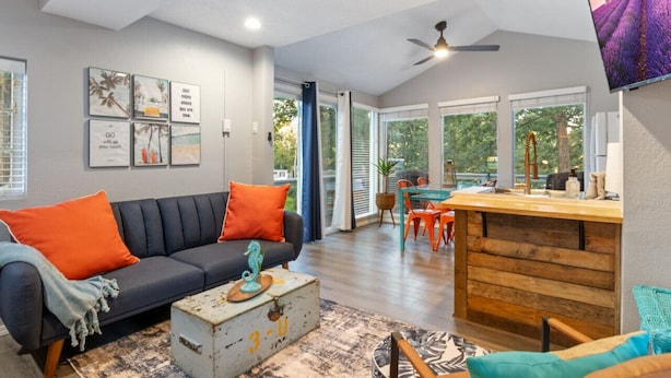 Un salon moderne avec un canapé foncé, des coussins orange, une table basse en bois et un coin repas avec des chaises orange.