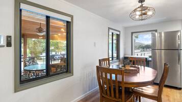 A dining area with a round table, wooden chairs, a chandelier, and a stainless steel refrigerator.