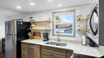 A modern kitchen with a stainless steel refrigerator, a coffee maker, and a window with a view of a dock and water.