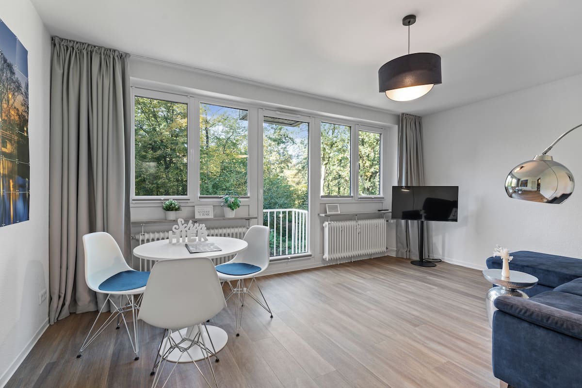 A modern living room with a dining area, large windows, a flat-screen TV, and a blue sofa.