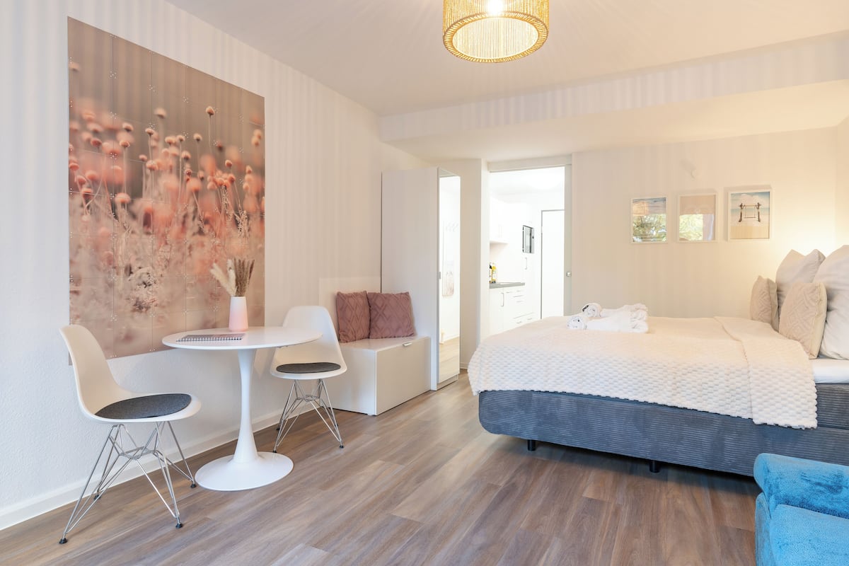 A modern hotel room with a large bed, a seating area with a table, and a large floral artwork on the wall.