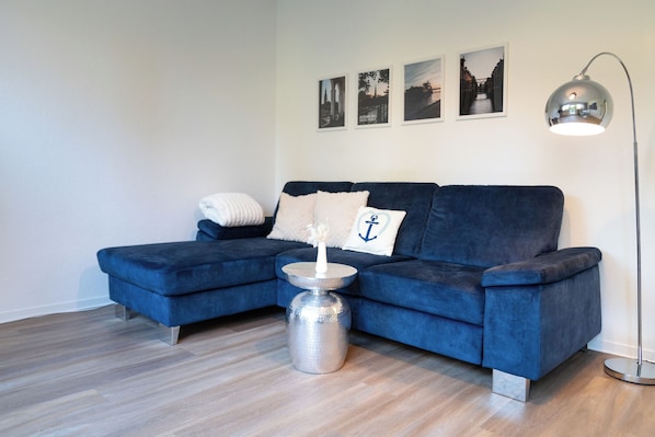 A modern living room with a blue sectional sofa, a metallic side table, and a floor lamp. - Ankerherz Gäste-Appartements (Hamburg)