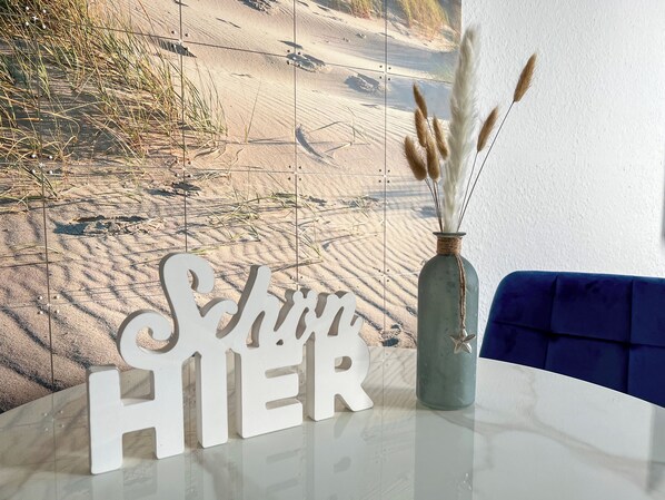 A table with a decorative sign spelling "SAND HIER" and a vase with pampas grass. - Ankerherz Gäste-Appartements (Hamburg)