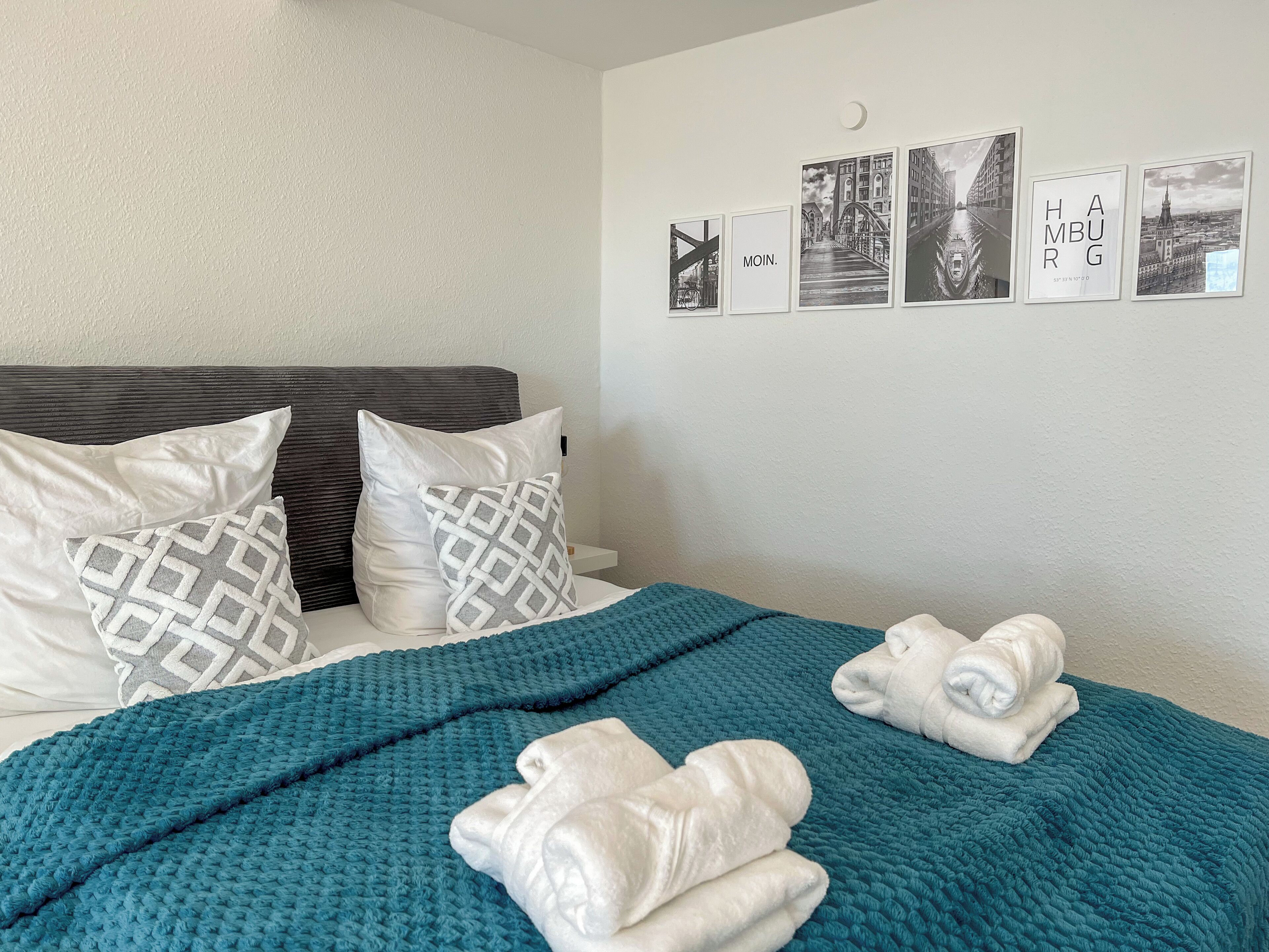 A neatly made bed with a teal blanket, white pillows, and folded towels.
