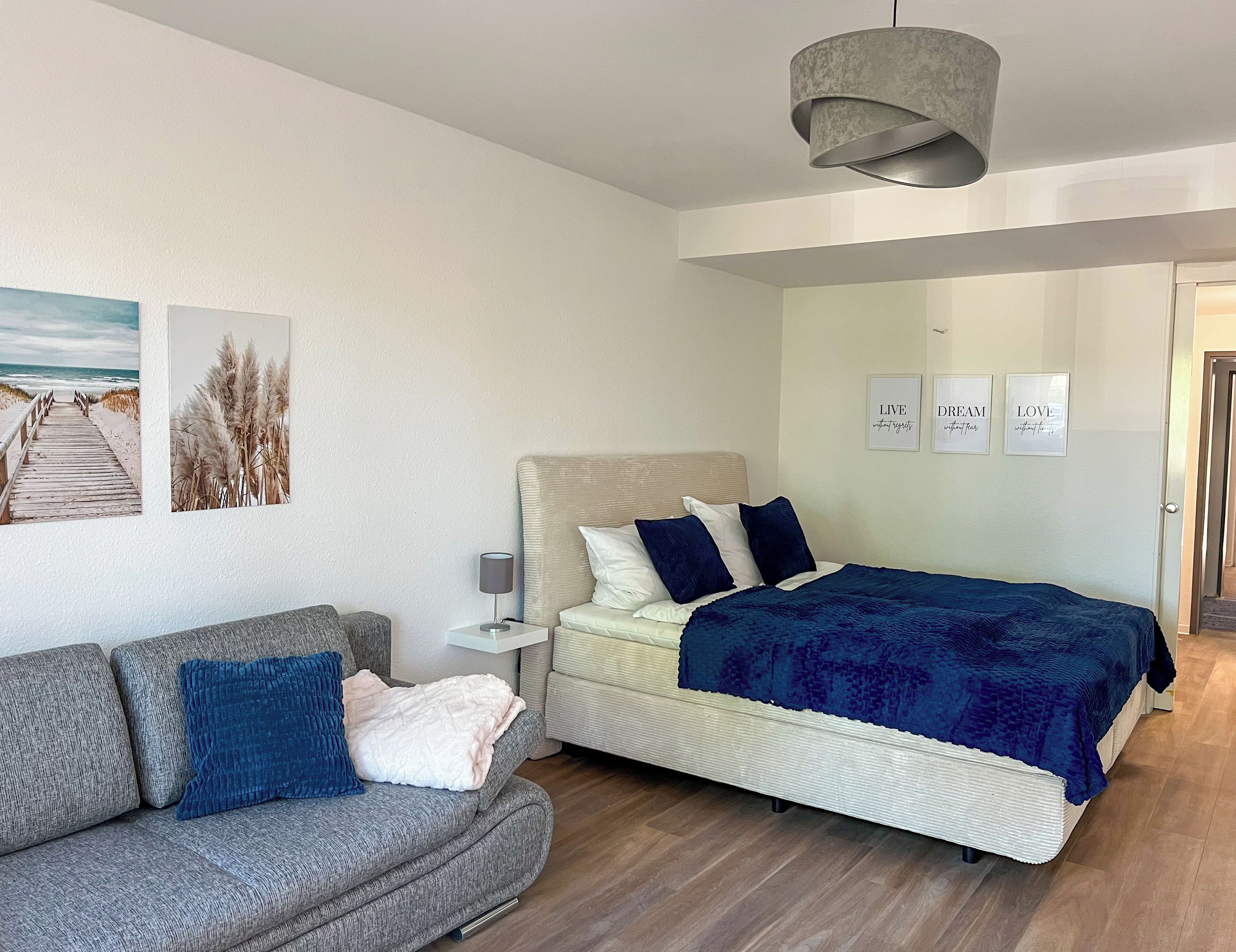 Une chambre à coucher avec un lit, un canapé gris, une table de chevet et des œuvres d’art murales.