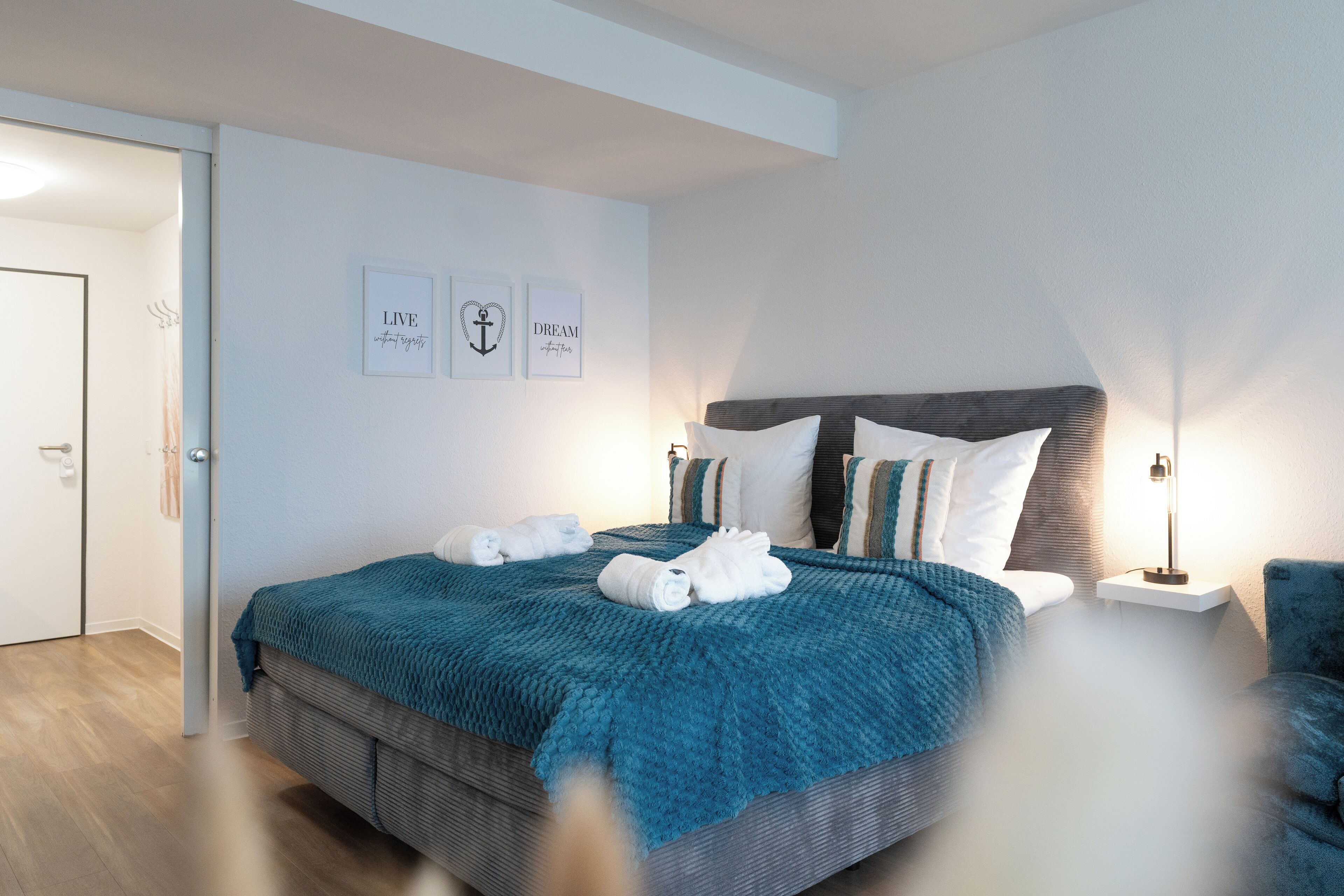 A modern bedroom with a large bed, a bedside table, and a nightstand. There are two framed motivational quotes on the wall.