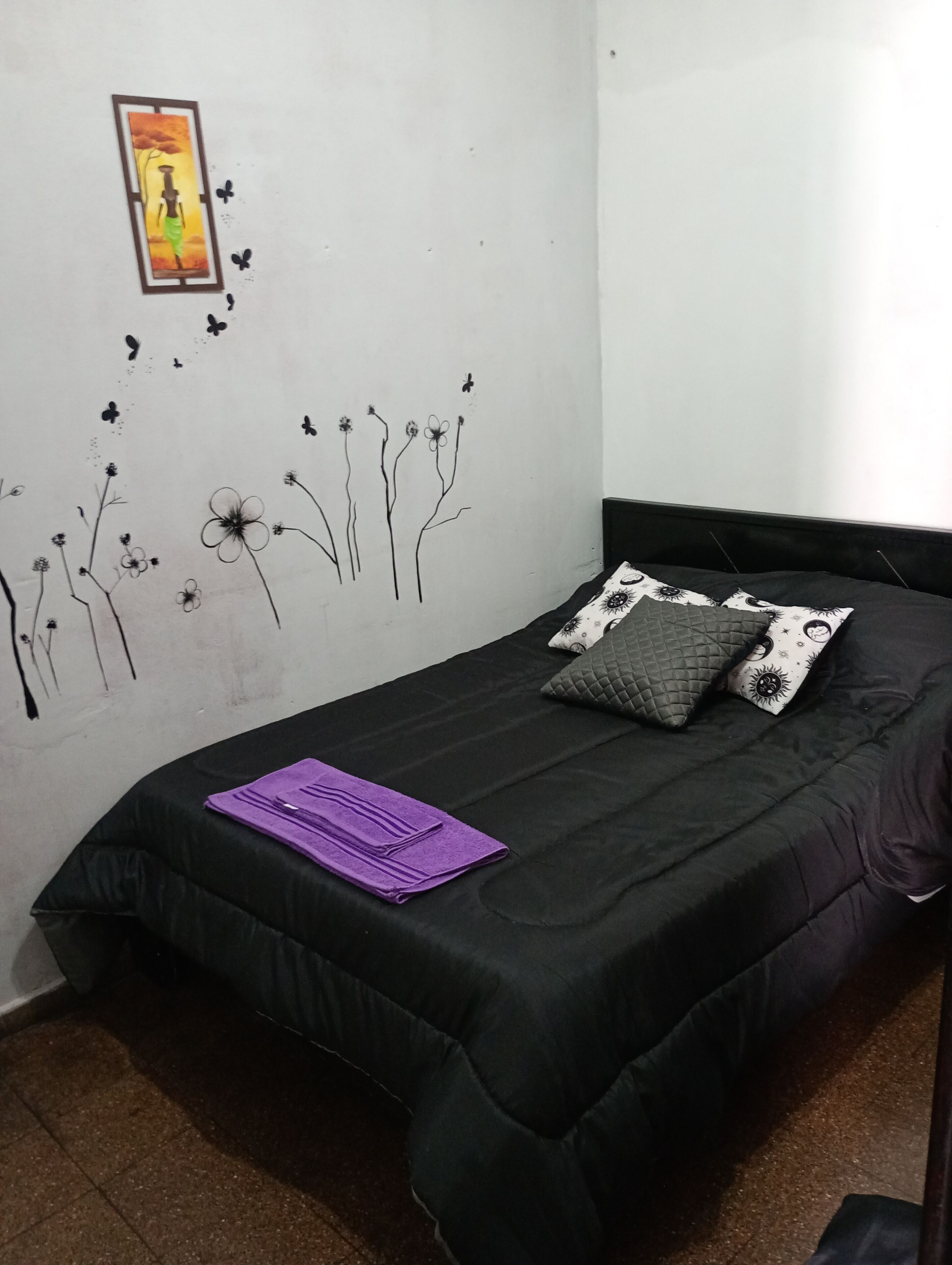A bedroom with a black bed, a purple towel, and a wall mural of trees and flowers.