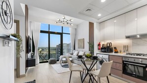 Una cocina moderna con estufa, microondas y fregadero. Hay una zona de comedor con mesa y sillas, y un gran ventanal con vistas a la ciudad.