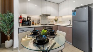 Una cocina moderna con armarios blancos, un refrigerador de acero inoxidable y una mesa de comedor con platos negros y un tazón de manzanas verdes.