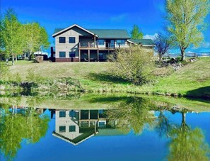 A two-story house with a balcony, a pond in front, and trees around. - Winter Dream Getaway (Kremmling)