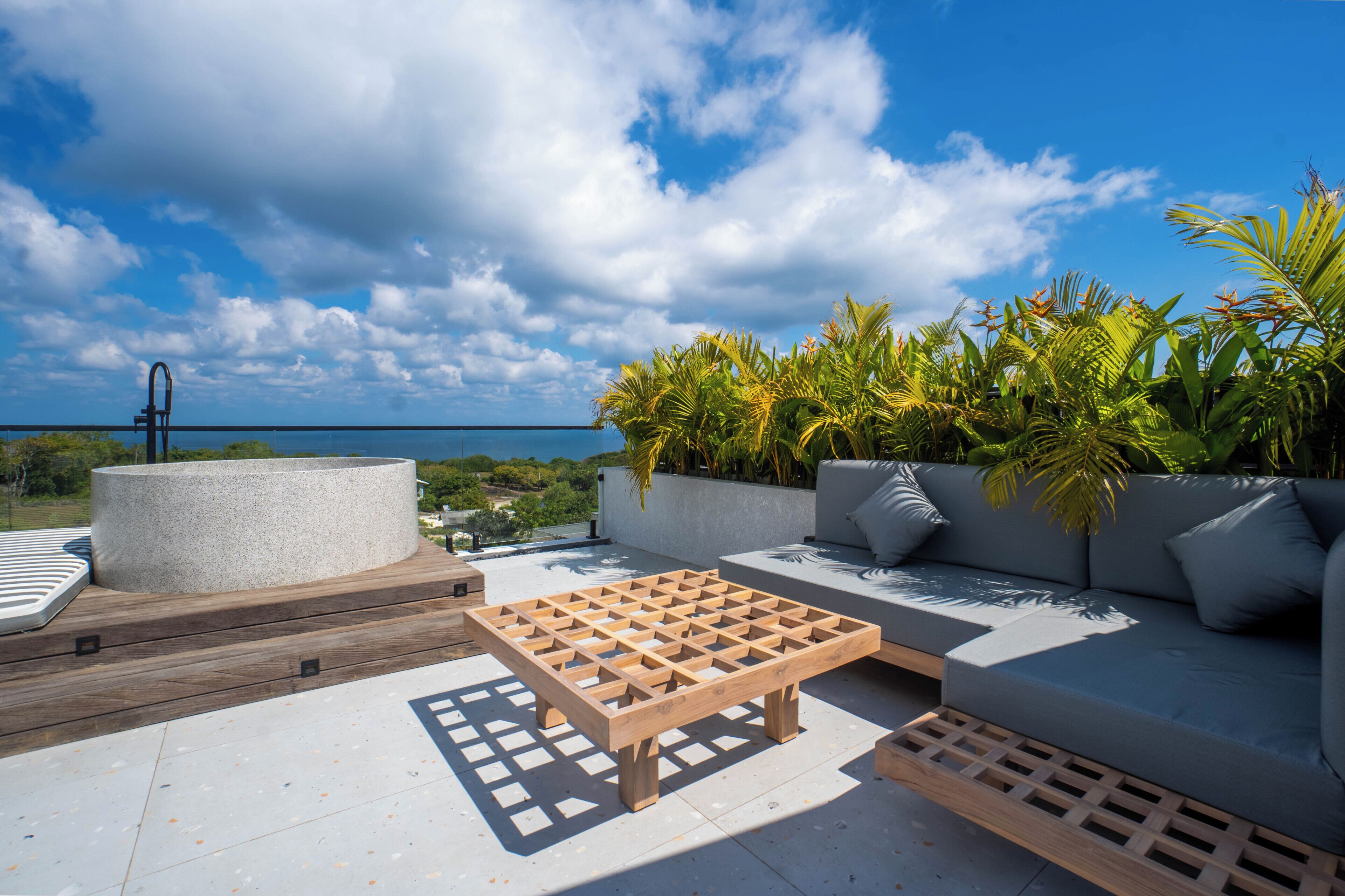 Una terraza en la azotea con una mesa de madera, un sofá y una maceta con plantas tropicales.