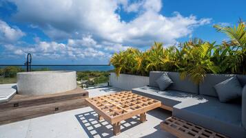 Una terraza en la azotea con una mesa de madera, un sofá y una maceta con plantas tropicales.