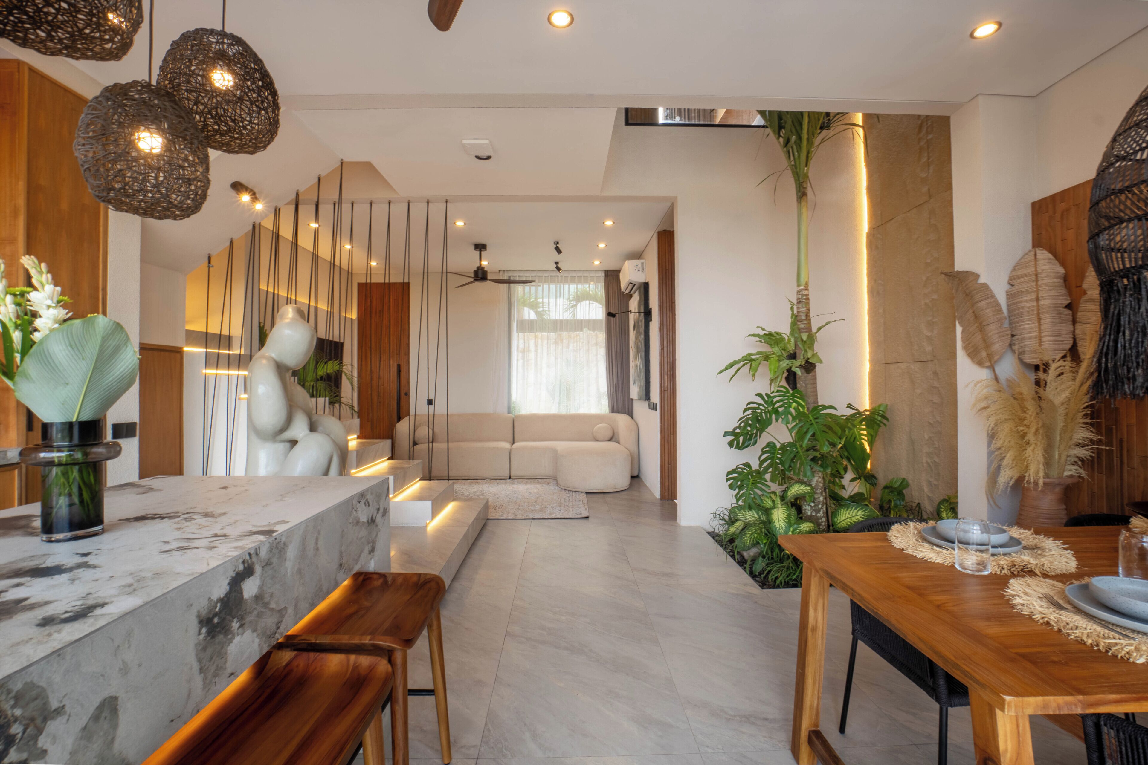 A modern interior with a marble countertop, wooden bar stools, a sofa, and a dining table with a woven placemat.