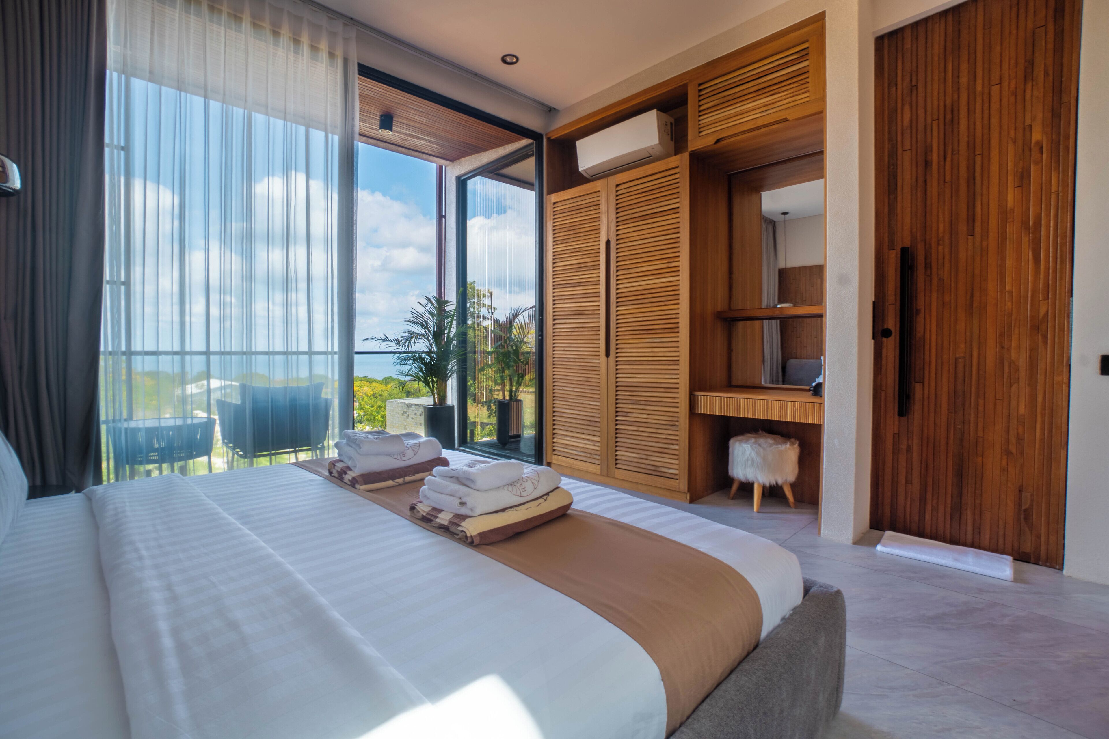 A modern bedroom with a large bed, a wooden wardrobe, and a balcony with a view.