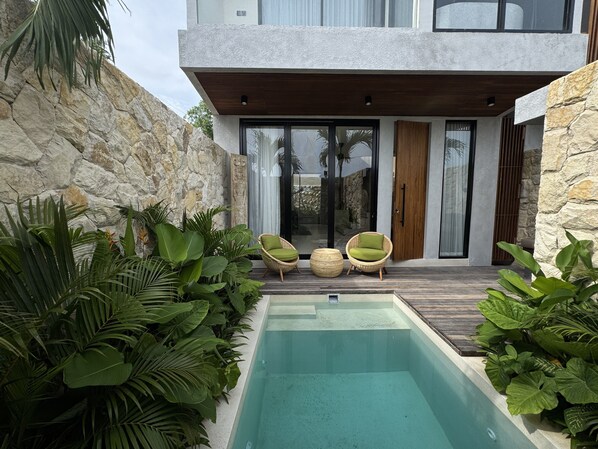 Une maison moderne dotée d’une piscine, de murs en pierre et de plantes tropicales.
