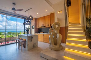A modern kitchen with wooden cabinets, a central island, and a large window overlooking a scenic view. - Rahya Villas Complex (Kutuh)