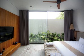 Une chambre moderne dotée d’une grande télévision, d’un lit, d’un banc et offrant une vue sur la verdure grâce à une porte-fenêtre coulissante.