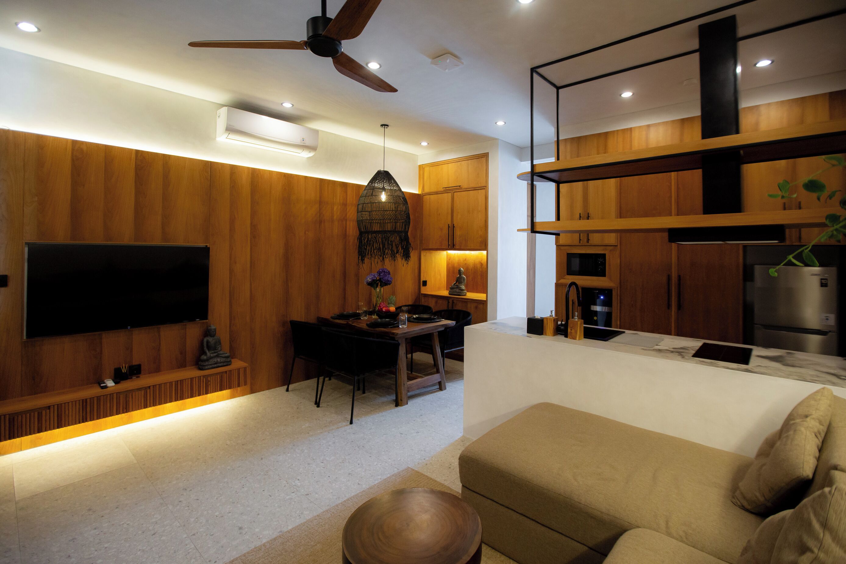 A modern living room with a sofa, a dining area with a table and chairs, a TV mounted on the wall, and a kitchen area with cabinets and appliances.