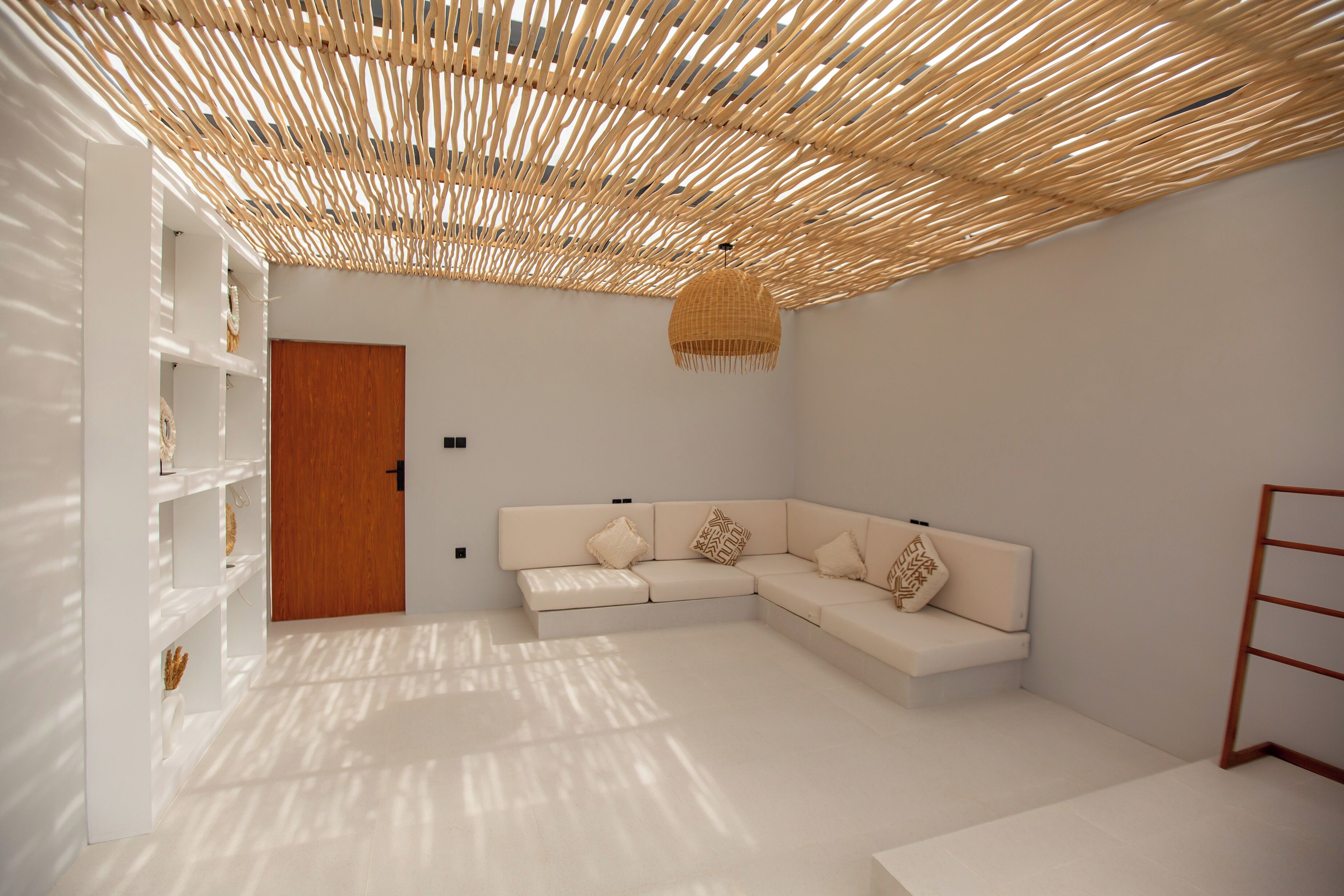 Une pièce moderne et minimaliste, avec un canapé blanc, une porte en bois et un plafond en osier.
